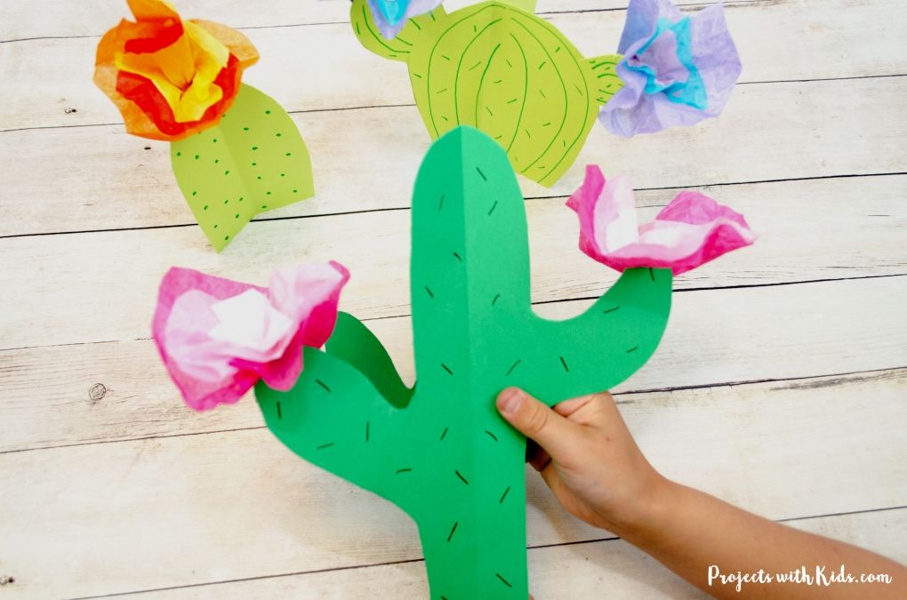Hand holding a 3D paper cactus with pink tissue paper flowers.