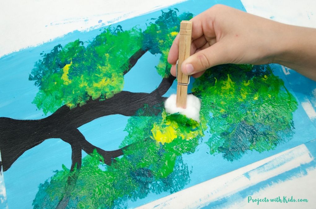 A hand painting leaves on an apple tree art project using a cotton ball to paint a light shade of green.