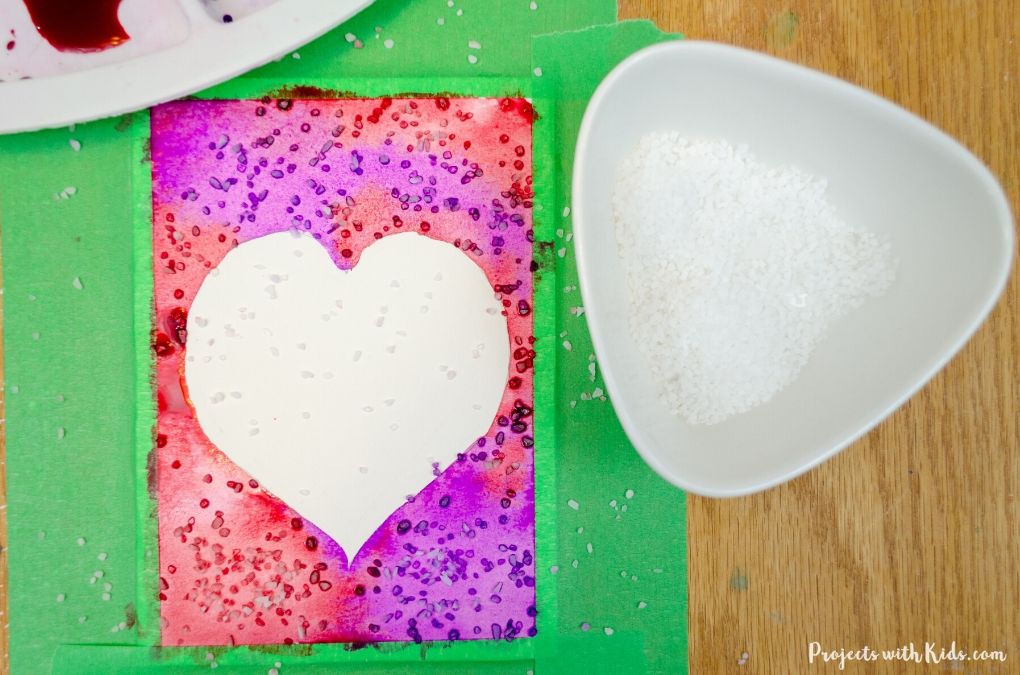 Sprinkling salt onto a watercolor Valentine's Day card art project for kids.