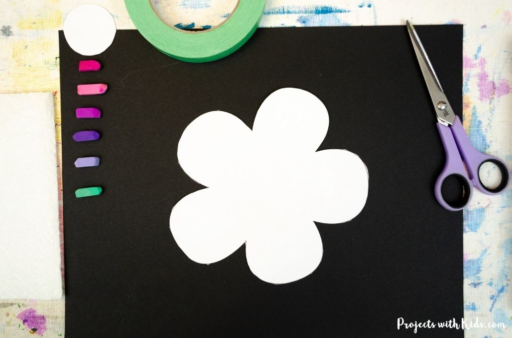 Taping a flower template to black drawing paper