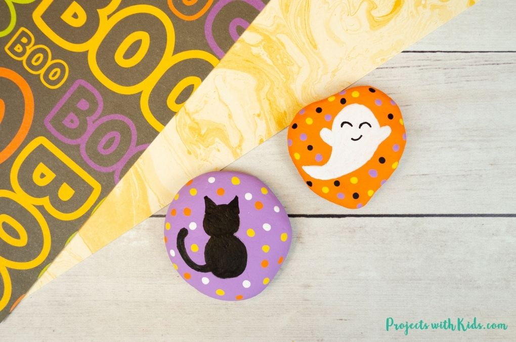 Black cat and ghost painted Halloween rocks kids craft idea.