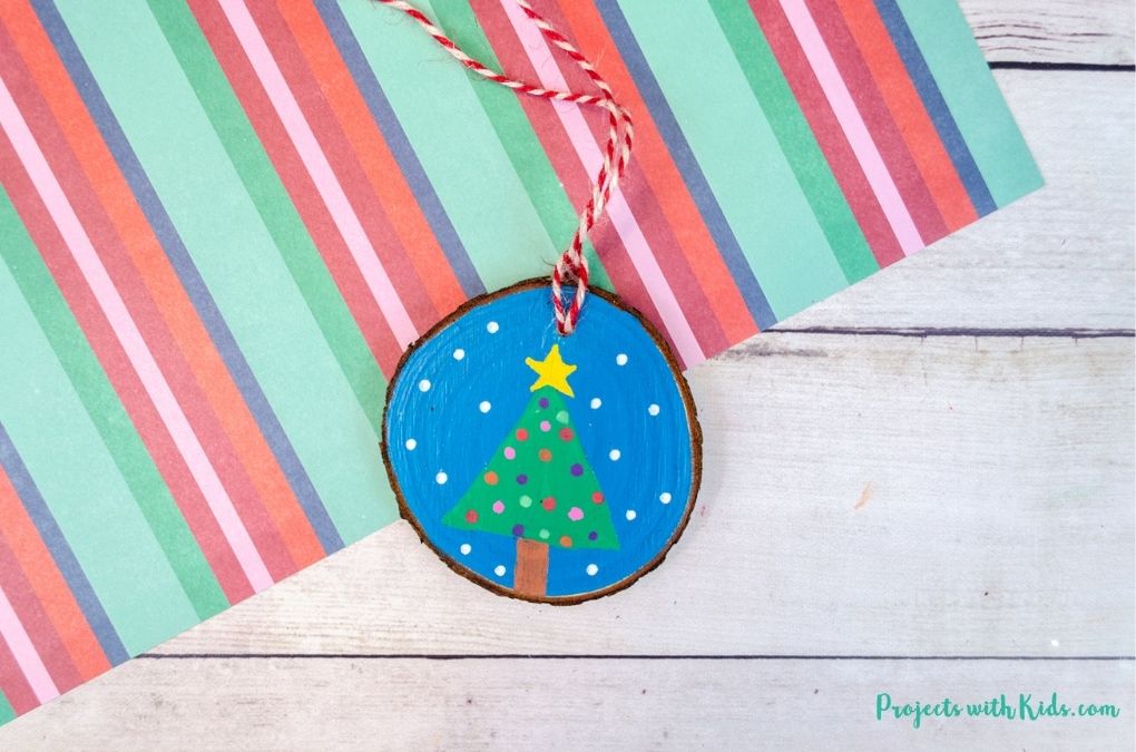 Wood slice ornament painted with a christmas tree and snow.