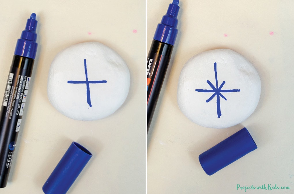 Drawing a snowflake design on a white painted rock with a blue paint pen