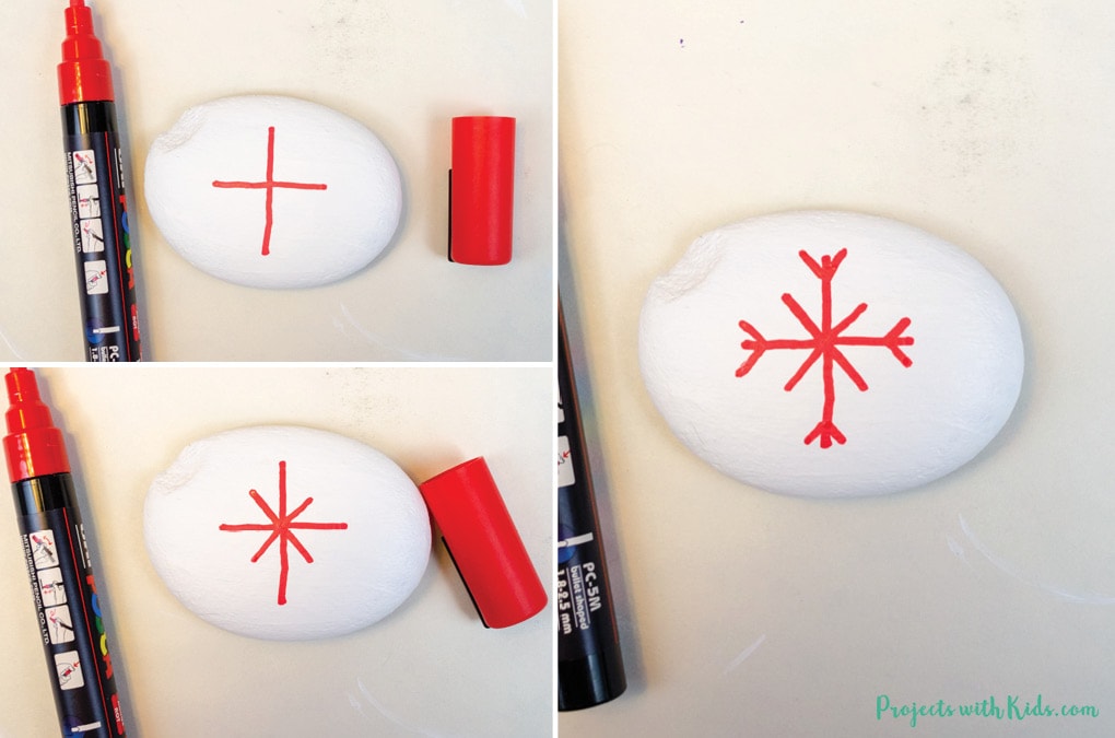 Drawing on a snowflake design on a rock using a red paint pen.