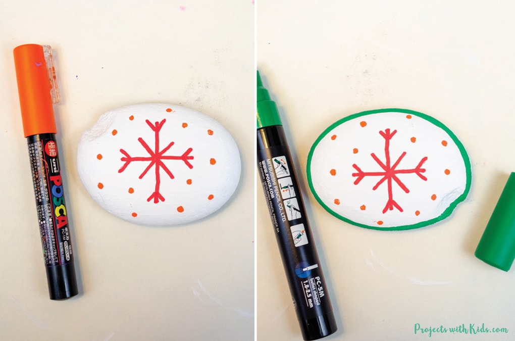 Drawing on details to a snowflake rock with paint pens for a winter craft idea for kids