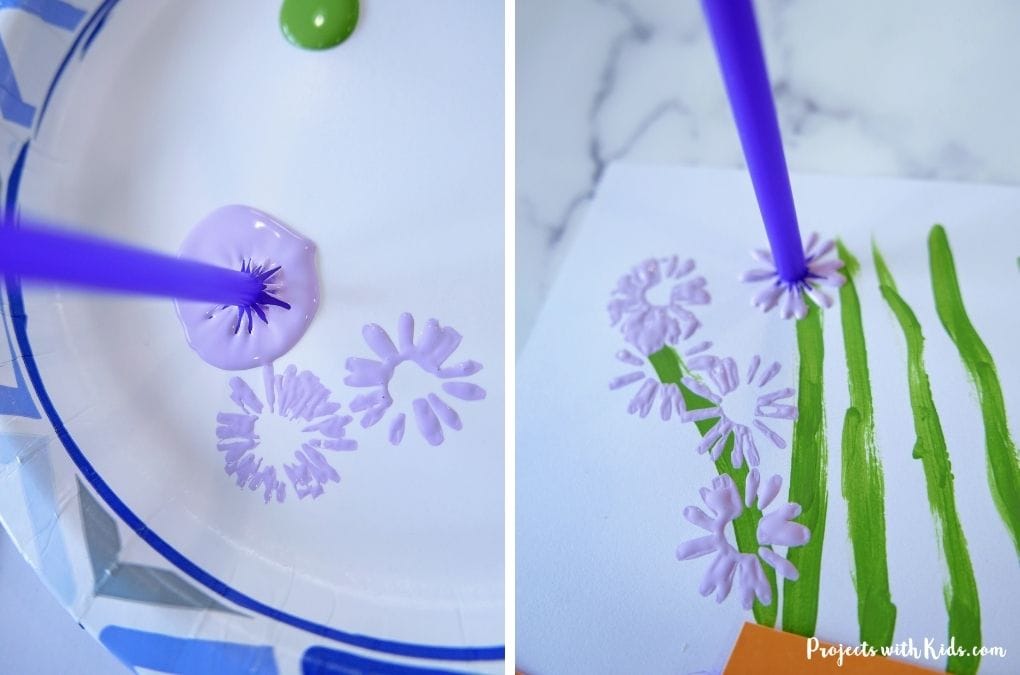 Using a straw to paint pale purple flowers on paper