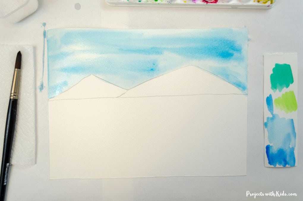 Painting in a blue sky using a wet on wet watercolor technique.