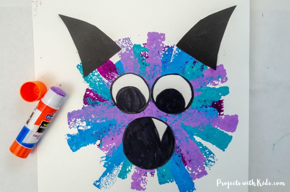 Gluing eyes, mouth and horns onto a monster painting. Halloween kids craft.