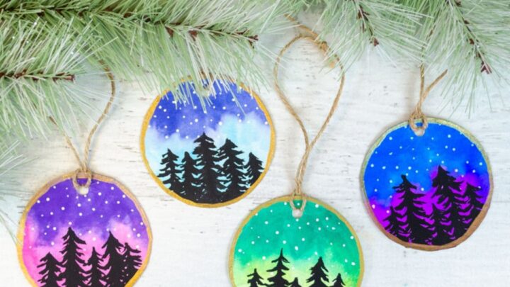 Watercolor Christmas ornaments with colorful sky and black trees with stars.