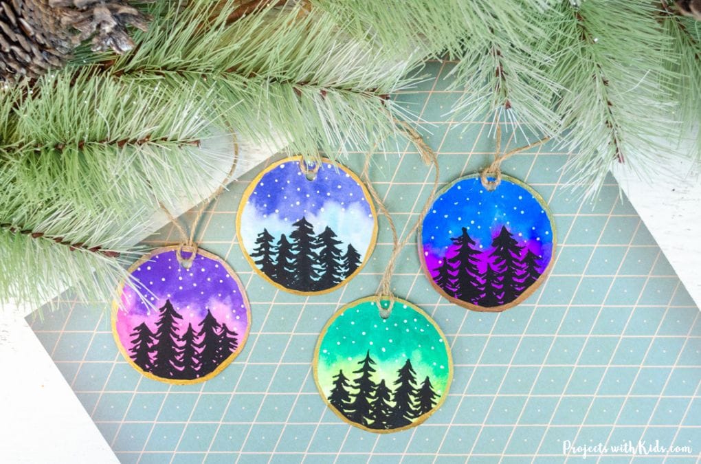 Watercolor Christmas ornament art project for kids with colorful sky, black trees, stars