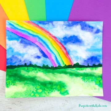 Watercolor rainbow painting idea for kids. Rainbow in a stormy sky with grass.