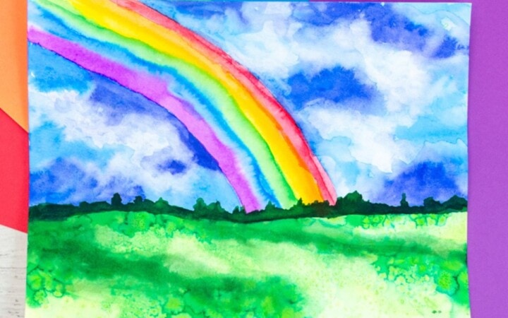 Watercolor rainbow painting idea for kids. Rainbow in a stormy sky with grass.