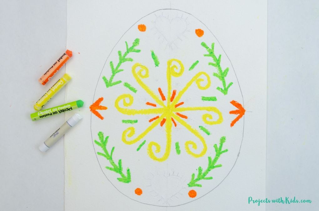 Drawing a design with oil pastels on an Easter egg template on watercolor paper.
