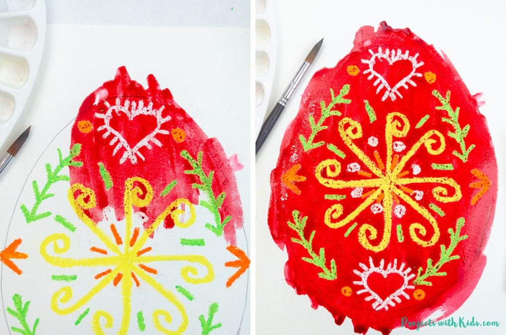 Painting red watercolor paint over oil pastels to create a Ukrainian Easter egg art project.