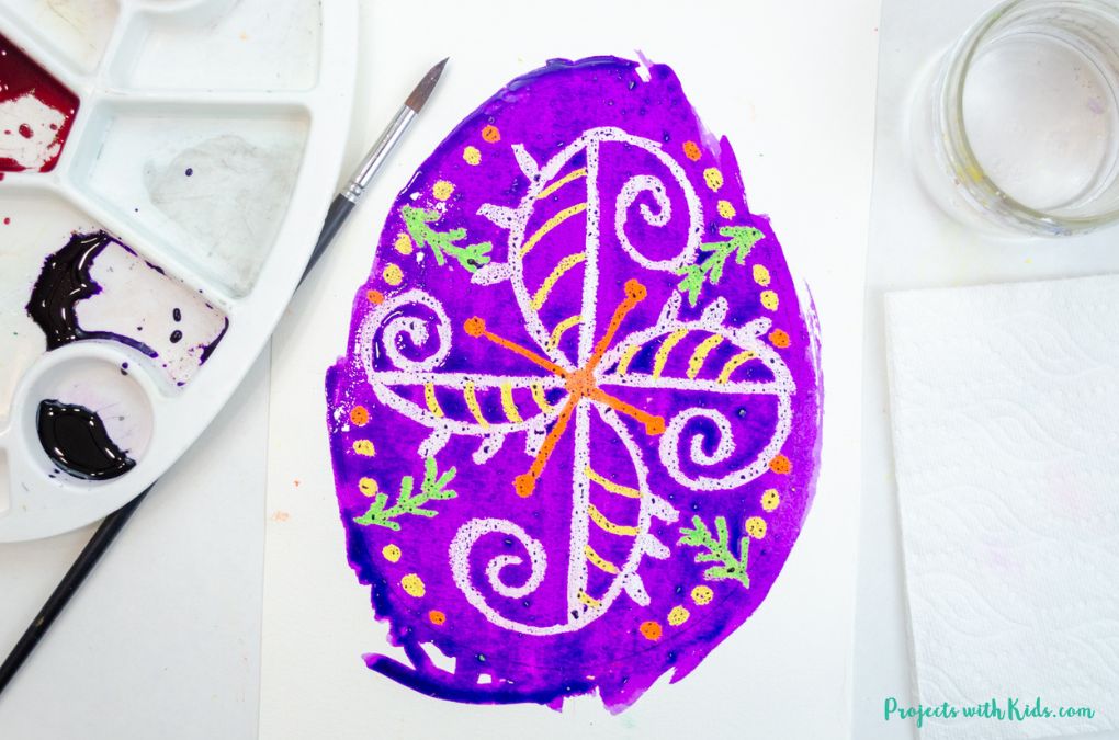Painting purple watercolor over oil pastels to make a Ukrainian Easter egg art project for kids.